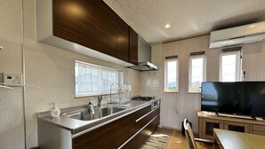 A modern kitchen with a stainless steel sink, wooden cabinets, a built-in stove, and a large flat-screen TV. - shirahamakashibessoD-157 (Shirahama)