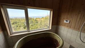 A bathroom with a freestanding bathtub, a window with a view of trees and mountains, and a tiled floor. - shirahamakashibessoD-157 (Shirahama)