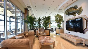 A spacious lobby with a large sofa, a coffee table, and a TV on a marble console. - Fevzi Hoca Hotel (Akçaabat)