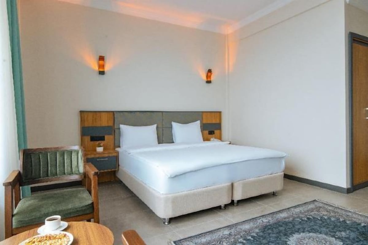 A hotel room with a bed, bedside tables, a chair, a small table with a plate of nuts, and a rug.