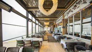 A restaurant with a long counter, multiple tables, and chairs. - Fevzi Hoca Hotel (Akçaabat)