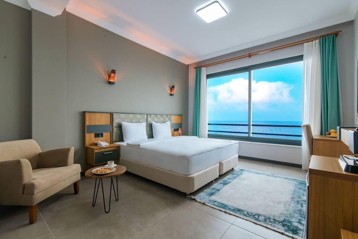 Quarto de hotel moderno com cama grande, sofá, escrivaninha e vista para o mar.