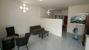 Een woonkamer met een bank, een glazen salontafel, een stoel, een televisie en een ventilator.