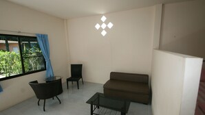 Een kamer met een bruine bank, een glazen tafel, een rieten stoel en een zwarte stoel.