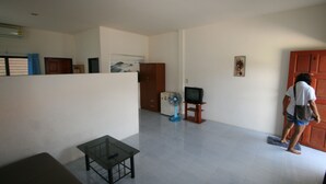 Een kamer met een glazen tafel, een ventilatorkachel, een televisie en een houten deur.