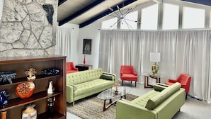 A living room with a stone wall, a green sofa, red chairs, and a glass coffee table. - Four king size bedrooms with 5 bathrooms and a pool with a view of Mt. Shasta (Redding)