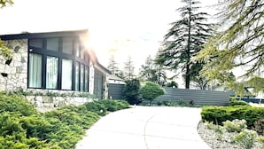 A pathway leading to a stone building with large windows, surrounded by well-maintained greenery and trees. - Four king size bedrooms with 5 bathrooms and a pool with a view of Mt. Shasta (Redding)