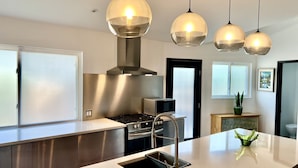 A modern kitchen with stainless steel appliances, a central island with a sink, pendant lighting, and a view of the living area. - Four king size bedrooms with 5 bathrooms and a pool with a view of Mt. Shasta (Redding)