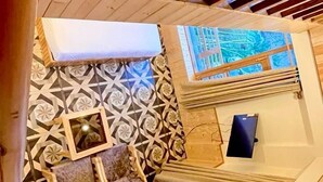 Una habitación con techo inclinado, vigas de madera, un papel tapiz con diseño, un pequeño rincón de descanso, una ventana y una piscina.