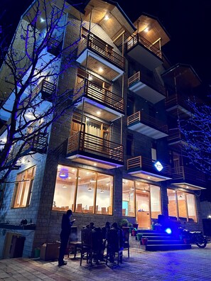 Un immeuble à plusieurs étages doté de balcons, de grandes fenêtres et d’un espace repas visible.