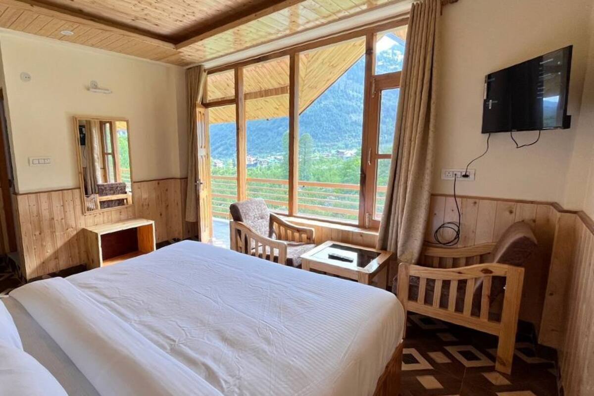 Une chambre d’hôtel avec un grand lit, un bureau, une chaise et une télévision. Il y a une fenêtre donnant sur les montagnes.