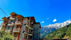 Un edificio de varios pisos con balcones, con montañas nevadas y un cielo azul despejado al fondo.
