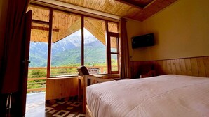 Un dormitorio con cama, un escritorio de madera y un amplio ventanal con vistas a la montaña.