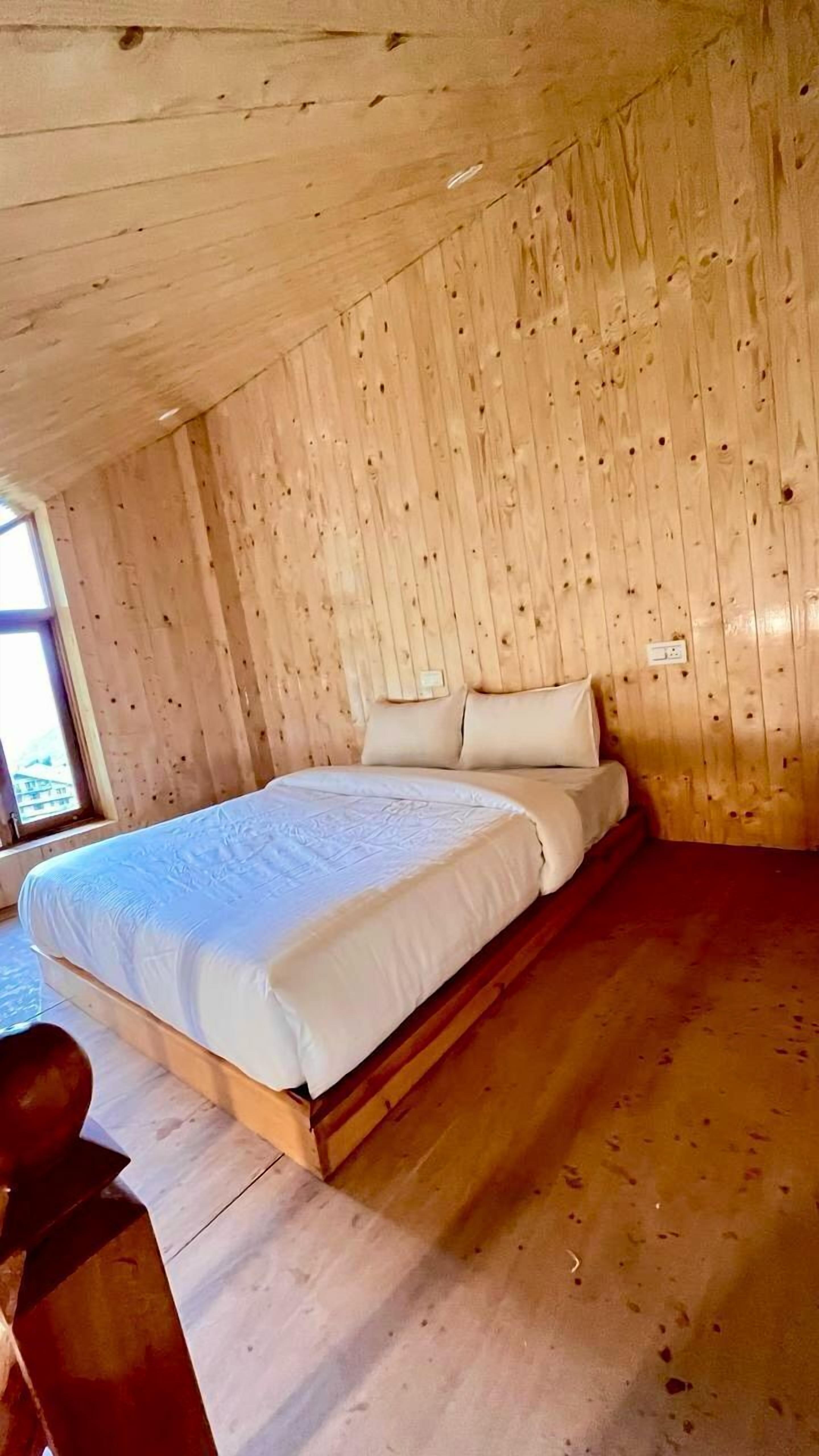 Une chambre dans une cabane en bois, avec un lit, des oreillers et une fenêtre.