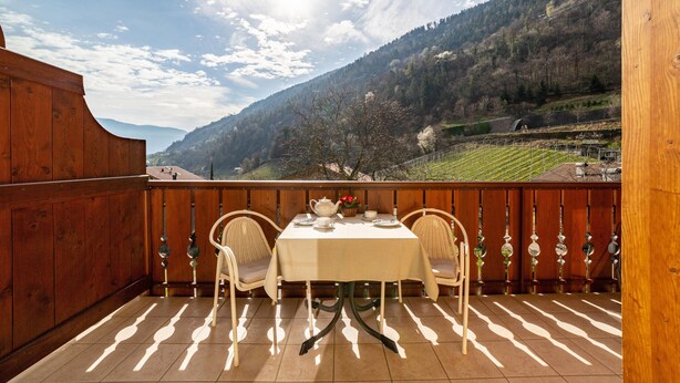 A wooden balcony with a table and chairs, overlooking a mountainous landscape. - Apartment 'Obermoarhof Ifinger' with Mountain View, Shared Garden and Wi-Fi (Lagundo)