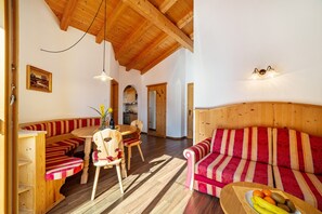 A wooden interior with a dining area, a sofa, and a kitchen in the background.