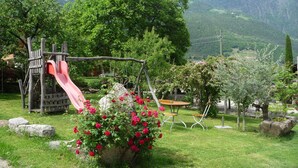 A playground with a slide, benches, and a flower bed with red flowers. - Apartment 'Obermoarhof Ifinger' with Mountain View, Shared Garden and Wi-Fi (Lagundo)
