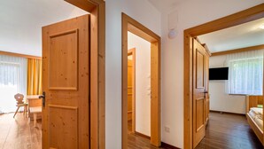 A room with wooden flooring, a bed, a TV, and a door leading to another room. - Apartment 'Obermoarhof Hönigspitze OG Deluxe' with Mountain View, Shared Garden and Wi-Fi (Lagundo)
