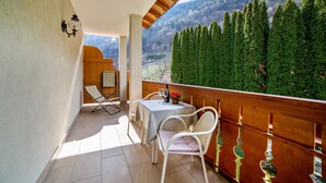 A balcony with a table and chairs, a view of a forested hillside, and a wooden railing. - Apartment 'Obermoarhof Hönigspitze OG Deluxe' with Mountain View, Shared Garden and Wi-Fi (Lagundo)