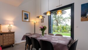 A dining area with a table set for six, a vase of flowers, pendant lights, a wooden dresser, and a painting on the wall.