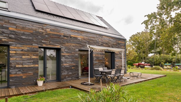 A modern house with a stone facade, a covered patio, and a solar panel roof.