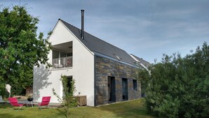 A modern house with a balcony, a chimney, and a small garden with grass and a tree.