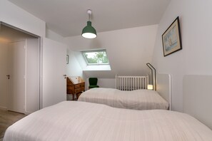 A bedroom with two beds, a window, a desk, a chair, and a crib.