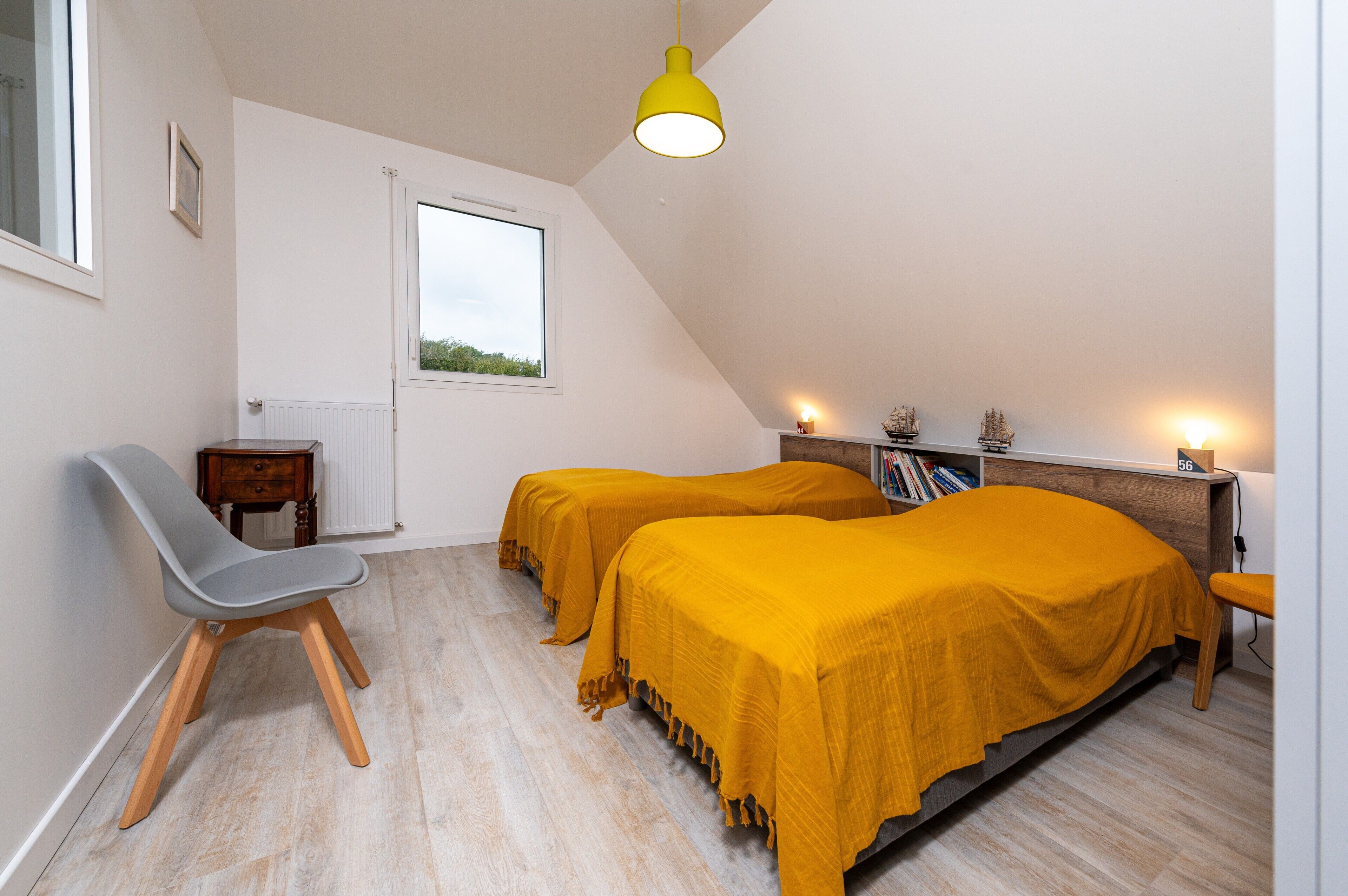 Een slaapkamer met twee bedden, een bureau, een stoel, een raam en een plafondlamp.
