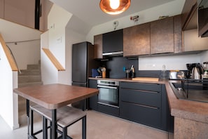 A modern kitchen with dark cabinetry, a built-in oven, and a wooden table.