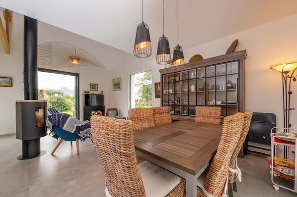 A dining area with a wooden table, wicker chairs, a cabinet with glass doors, and pendant lights.