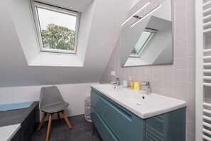 A modern bathroom with a skylight, a vanity with a mirror, and a chair.
