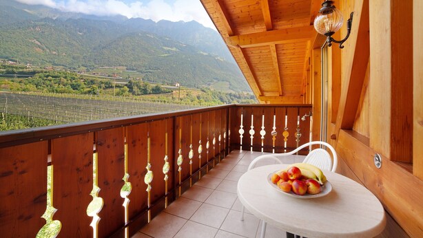 A wooden balcony with a table and chairs, a decorative light fixture, and a view of mountains. - Apartment 'Obermoarhof Hirzer' with Mountain View, Shared Garden and Wi-Fi (Lagundo)