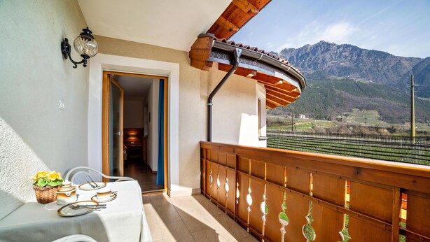 Uma varanda com vista para montanhas, uma mesa com cadeiras e guarda-corpo de madeira.