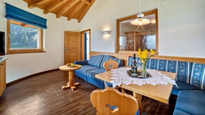 Um quarto aconchegante com teto de madeira, um sofá azul, uma mesa de jantar de madeira e uma janela com vista para árvores.