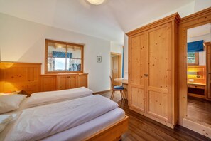 A bedroom with two beds, wooden wardrobe, and a window.