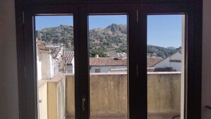 Une vue à travers une fenêtre, avec une montagne en arrière-plan, un toit recouvert de tuiles et un bâtiment à la façade blanche.