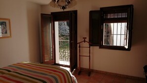 Une pi èce avec un lit, une fenêtre avec des volets, une porte donnant sur l’extérieur et un porte-manteau suspendu.