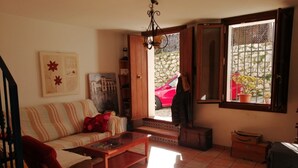 Un salon comprenant un canapé, un fauteuil, une table basse et une fenêtre donnant sur une voiture rouge et des plantes à l’extérieur.