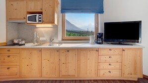 A kitchen with wooden cabinets, a microwave, a coffee maker, a TV, and a window with a view of a mountain. - Apartment 'Obermoarhof Mutspitze' with Mountain View, Shared Garden and Wi-Fi (Lagundo)