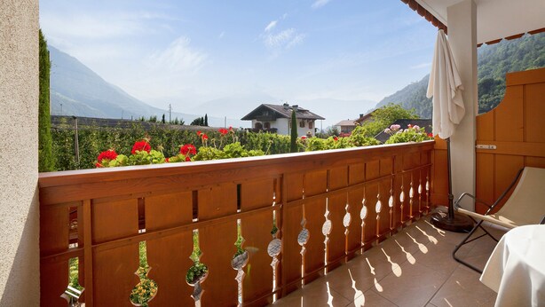 A balcony with a wooden railing, a table with a white tablecloth, and a view of a mountain and garden. - Apartment 'Obermoarhof Mutspitze' with Mountain View, Shared Garden and Wi-Fi (Lagundo)