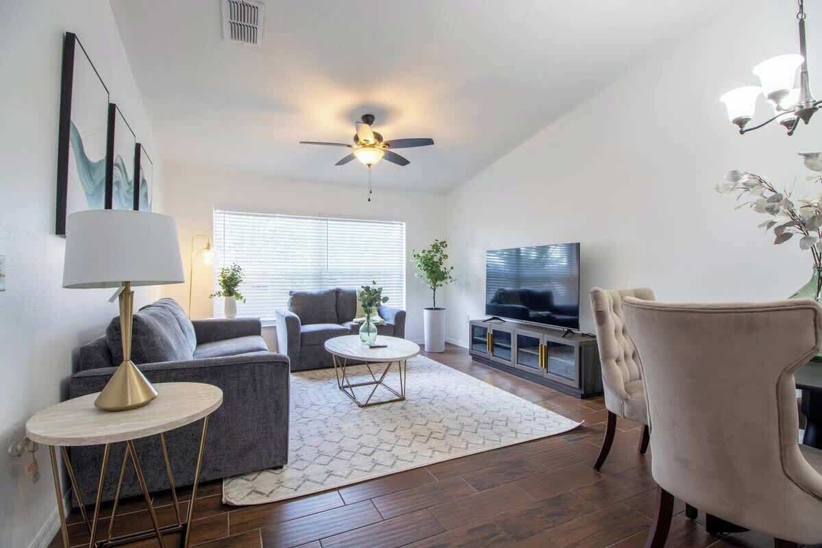 A modern living room with a grey sofa, a round coffee table, a TV, and a ceiling fan.