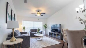 A modern living room with a grey sofa, a round coffee table, a TV, and a ceiling fan.