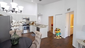 A modern kitchen with white cabinetry, stainless steel appliances, and a dining area with a dark table and chairs.