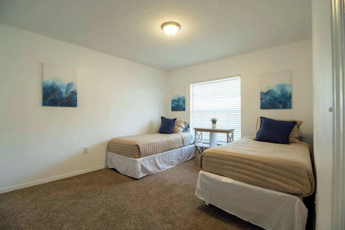 A room with two single beds, a small table, and two wall-mounted paintings.