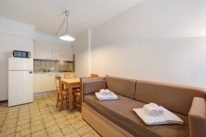 Un espacio habitable compacto con kitchenette, un sofá con toallas y una mesa de comedor.