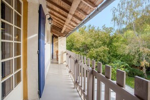 Eine überdachte Veranda mit Holzgeländer, einer blauen Tür und Blick auf Grünflächen.