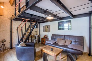 Un espace de vie de style industriel, avec des poutres apparentes, un escalier, un canapé et une table basse.