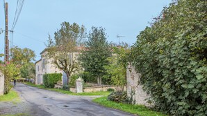 Un camino estrecho bordeado de vegetación y muros de piedra, que lleva a un edificio con fachada tradicional.