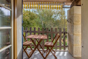 Un balcon avec une table et des chaises en bois, une clôture blanche en piquets et une vue sur les arbres et le ciel.