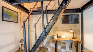 Una habitación con un escritorio de madera, una silla blanca, una escalera de metal, un mapa en la pared y un televisor.